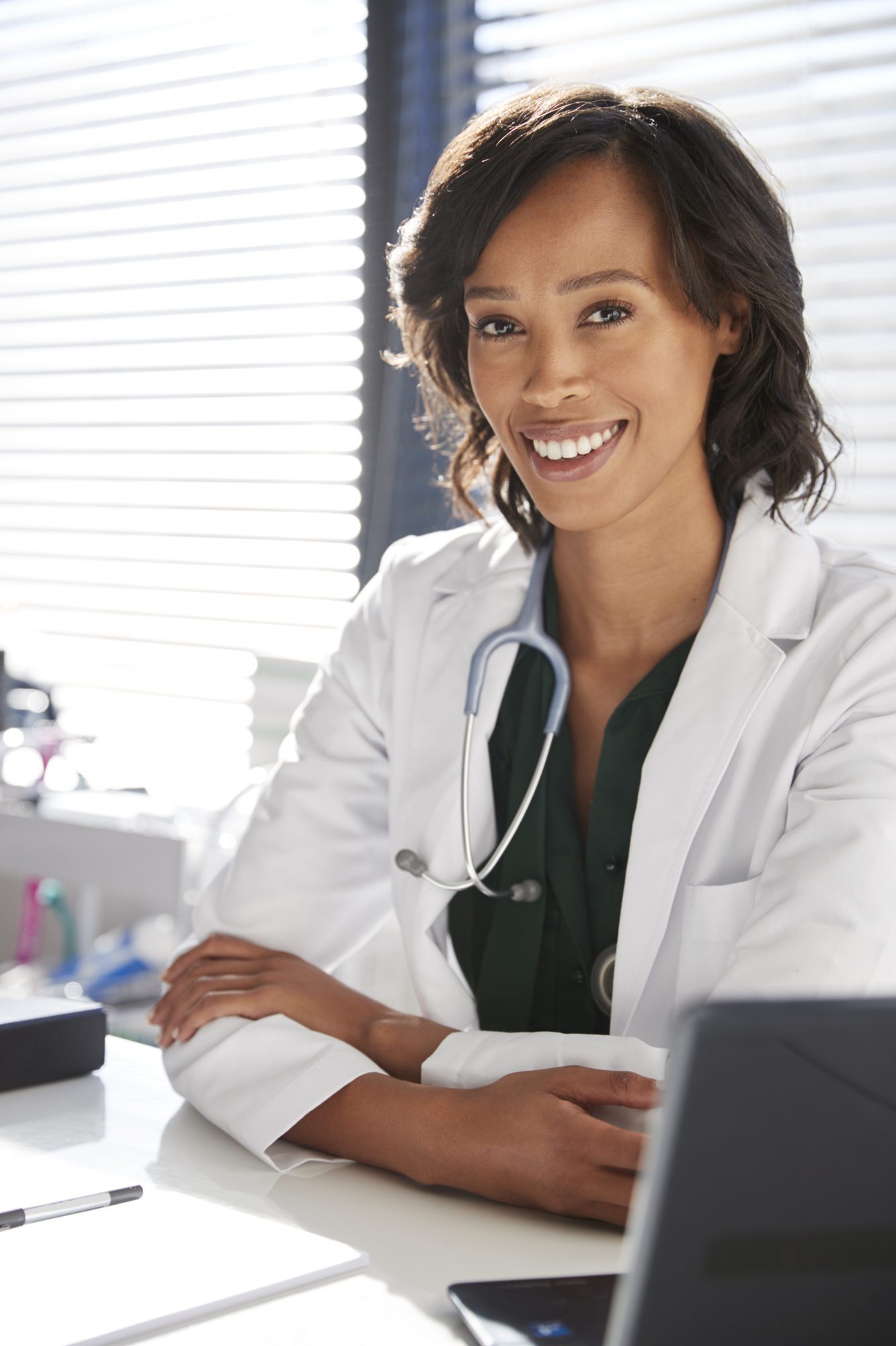 adobe stock image of Portrait Of Smiling Female Doctor Wearing White Coat With Stethoscope Sitting Behind Desk In Office